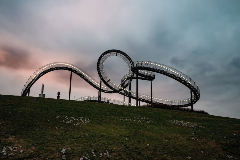 A large, circular metal structure on a grassy hill with a cloudy sky in the background.