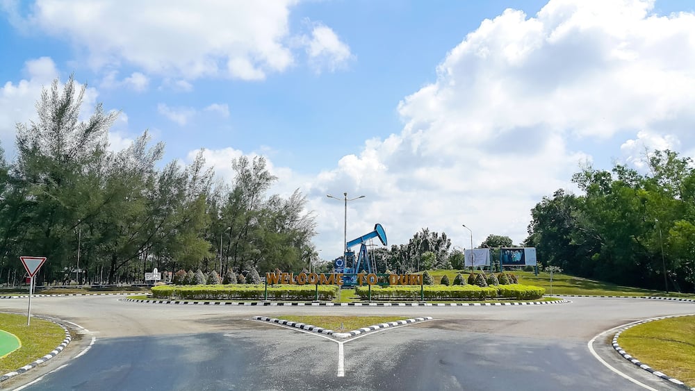 A roundabout with a blue oil pumpjack, surrounded by trees and greenery.
