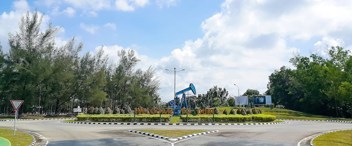 Crude oil pump jack monument at the crossroads with Duri city, Riau, Indonesia welcome sign. Clear blue sky.