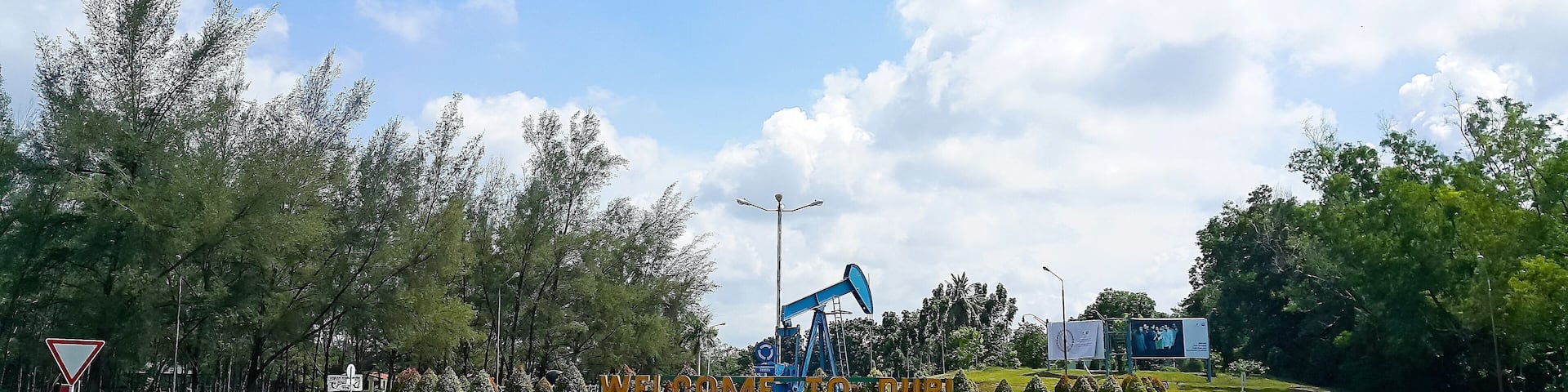 Crude oil pump jack monument at the crossroads with Duri city, Riau, Indonesia welcome sign. Clear blue sky.