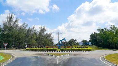 Crude oil pump jack monument at the crossroads with Duri city, Riau, Indonesia welcome sign. Clear blue sky.