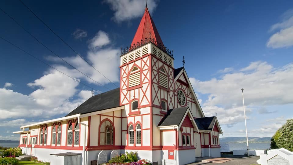 A church with a red and white facade, a tall steeple, and a view of the sea in the background.
