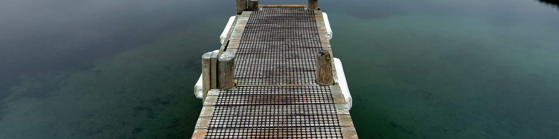 A calm lake with a wooden dock extending into the water, surrounded by forested hills.