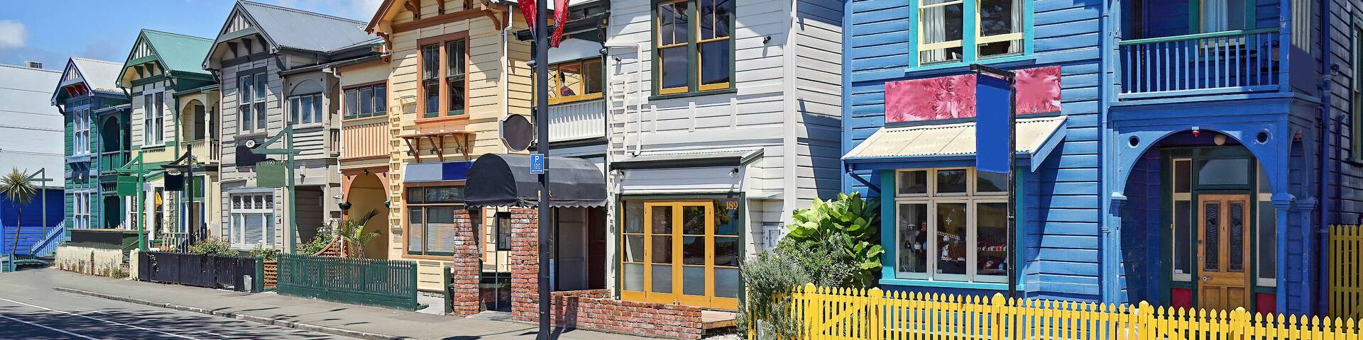 Colorful wooden buildings with distinct architectural styles, a street with a yellow fence, and a clear blue sky.