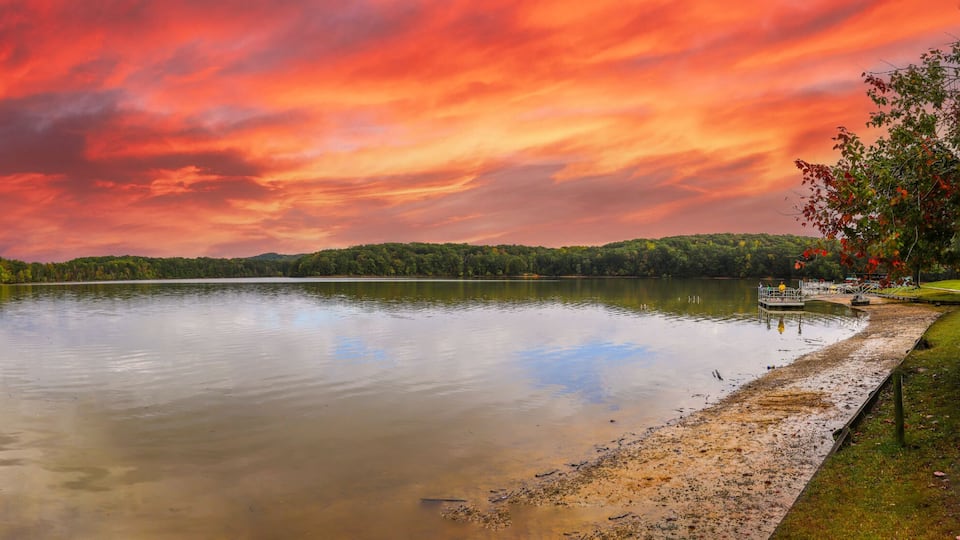a stunning panoramic shot of the silky brown waters of the Chattahoochee river surrounded by green and autumn colored trees with powerful clouds at Sweetwater Creek State Park in Lithia Springs GA