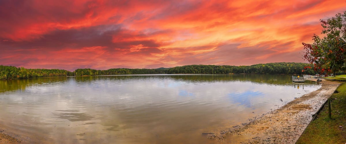 a stunning panoramic shot of the silky brown waters of the Chattahoochee river surrounded by green and autumn colored trees with powerful clouds at Sweetwater Creek State Park in Lithia Springs GA