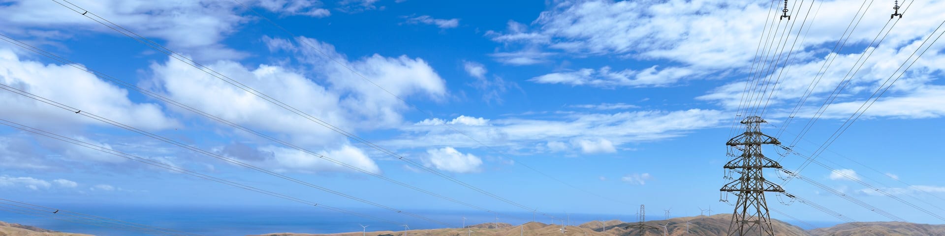 A hilly landscape with a dirt path, power lines, and wind turbines in the distance.