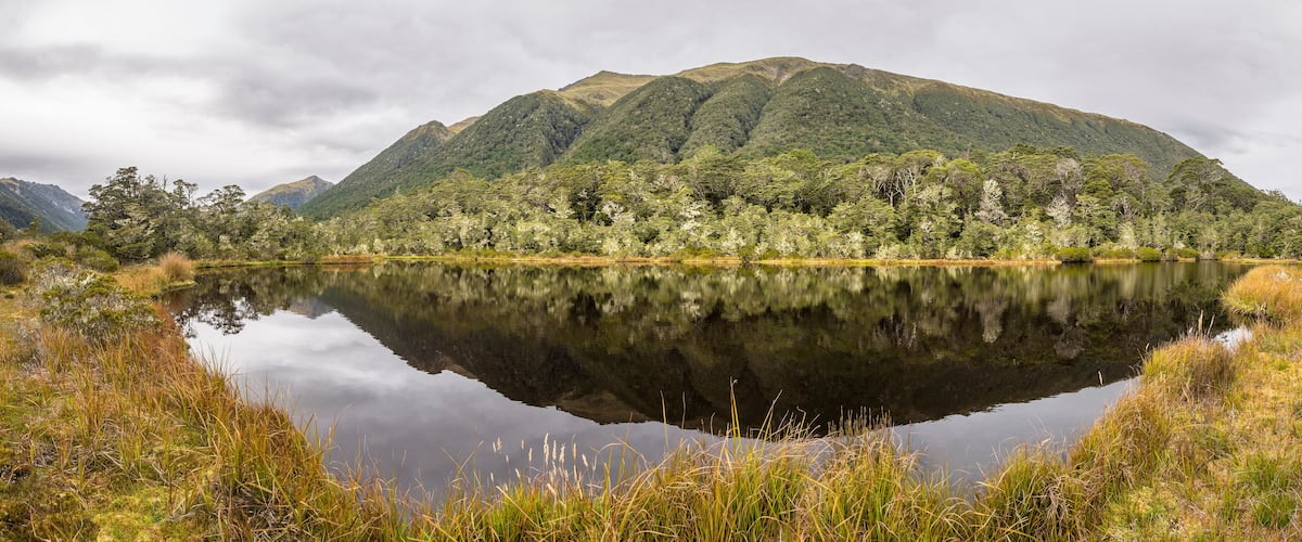 A calm lake reflecting a forested mountain range.
