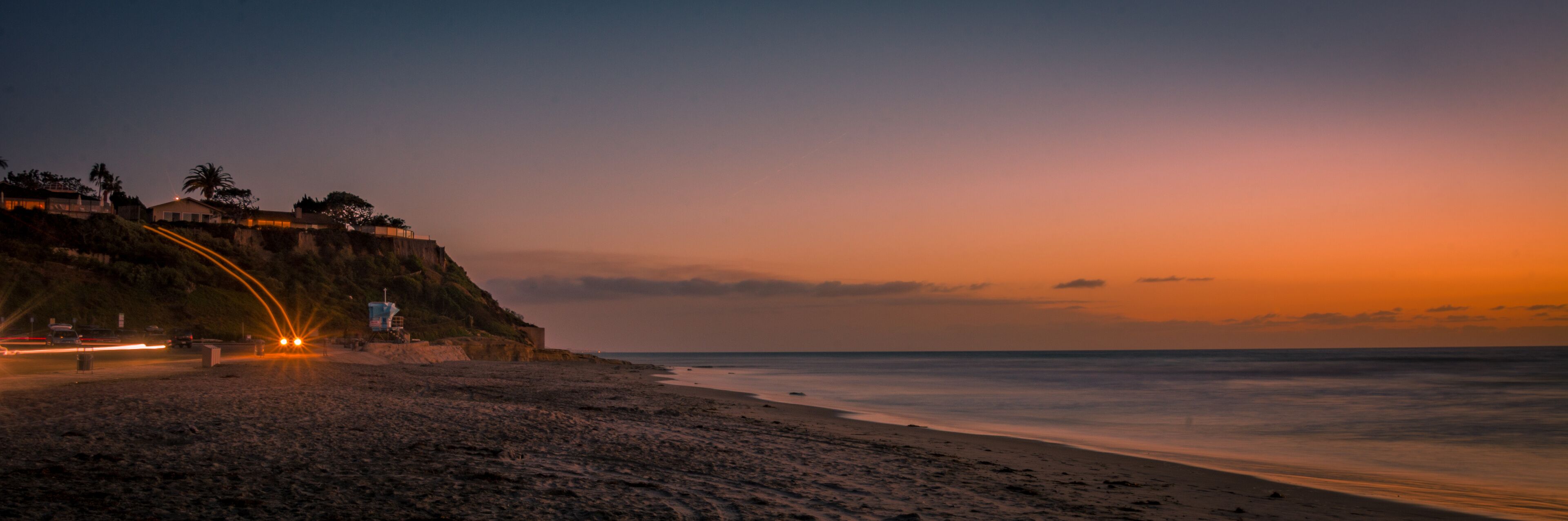 A beach at sunset with a cliff and a lifeguard tower.