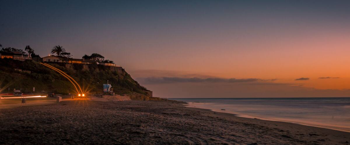 A beach at sunset with a cliff and a lifeguard tower.