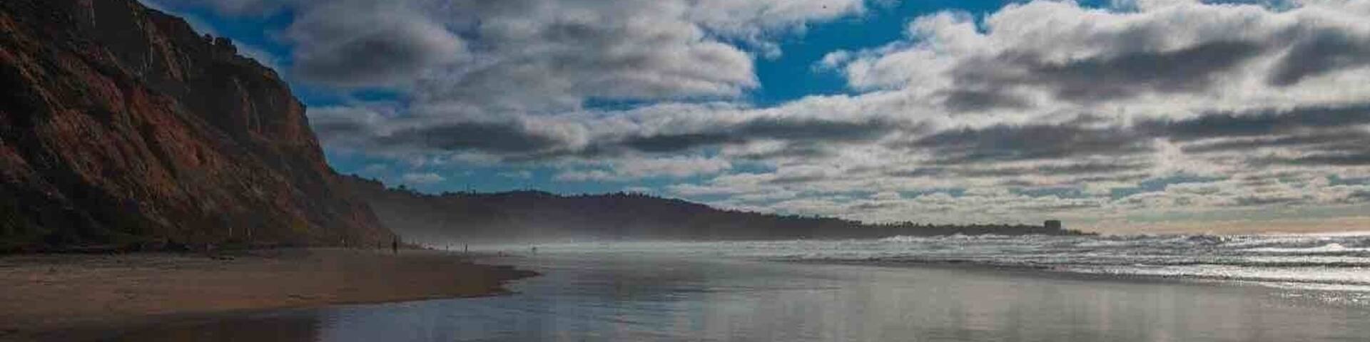 A beach with a rocky cliff on the left and a calm sea.