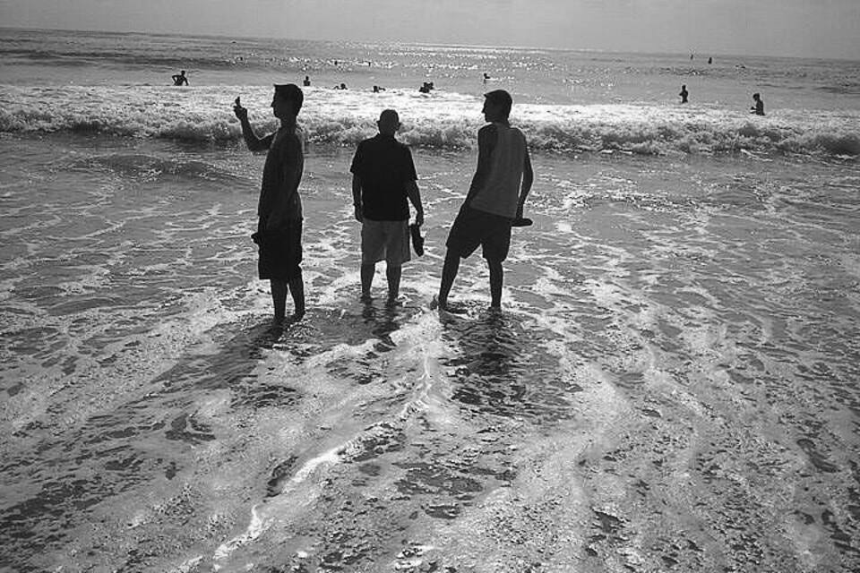 Three people standing on a beach with waves crashing onto the shore.
