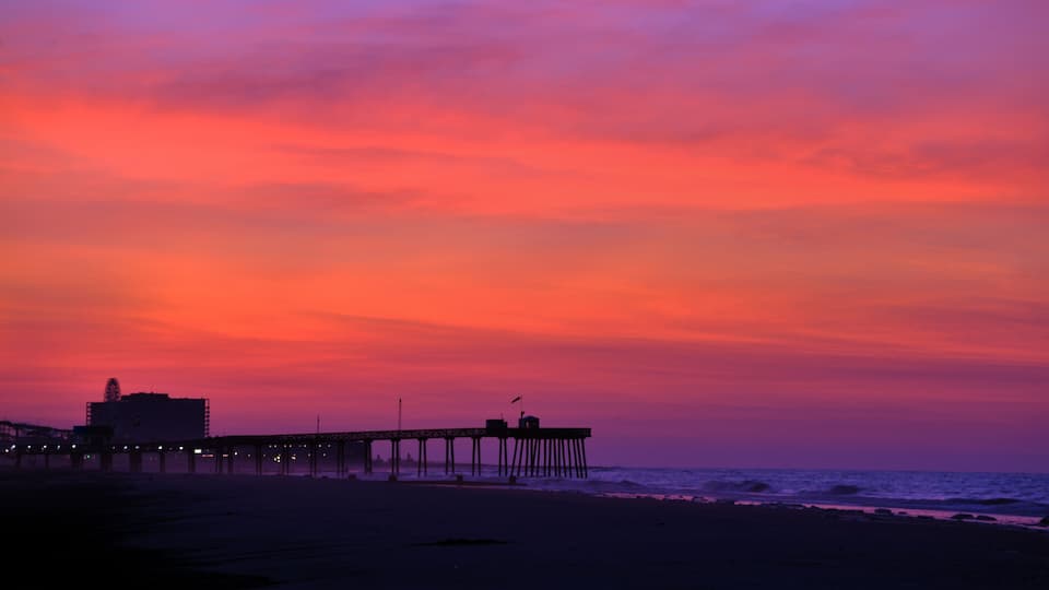 A pier extending into the ocean at sunset with a vibrant sky.