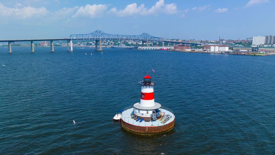 A lighthouse on a small island in the middle of a river, with a bridge in the background.