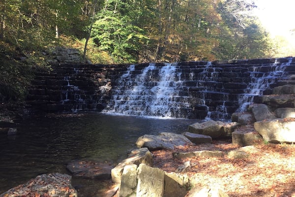 A waterfall cascading over a stone wall into a pond surrounded by rocks and trees.