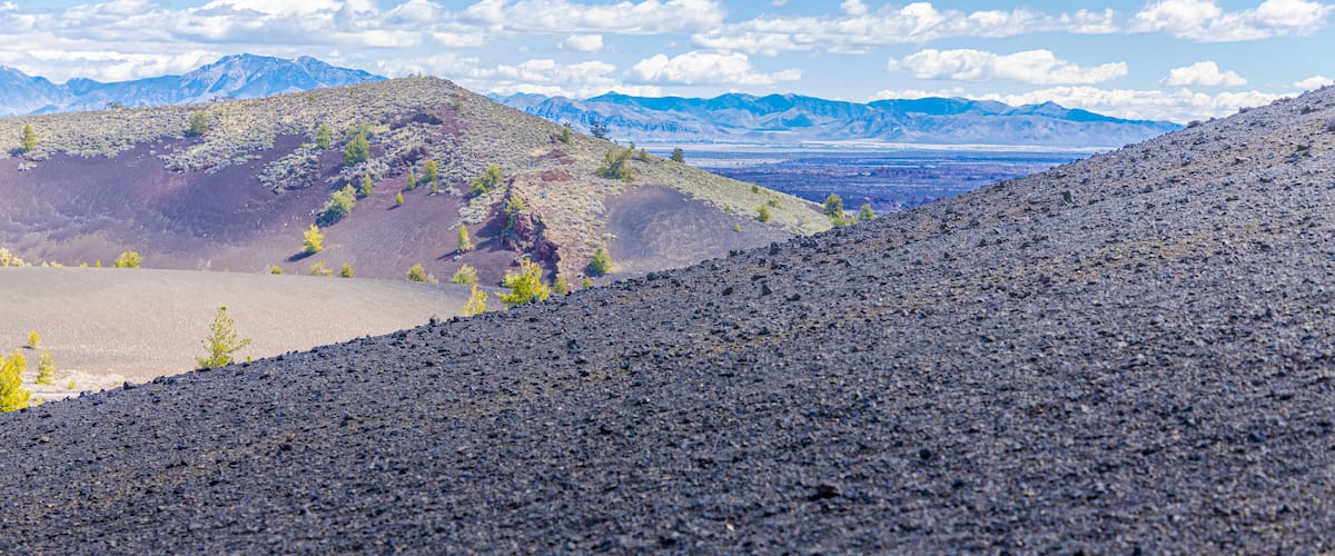 A volcanic landscape with rugged terrain and distant mountains under a clear sky.