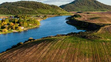 A river winding through a valley with fields on either side and hills in the distance.