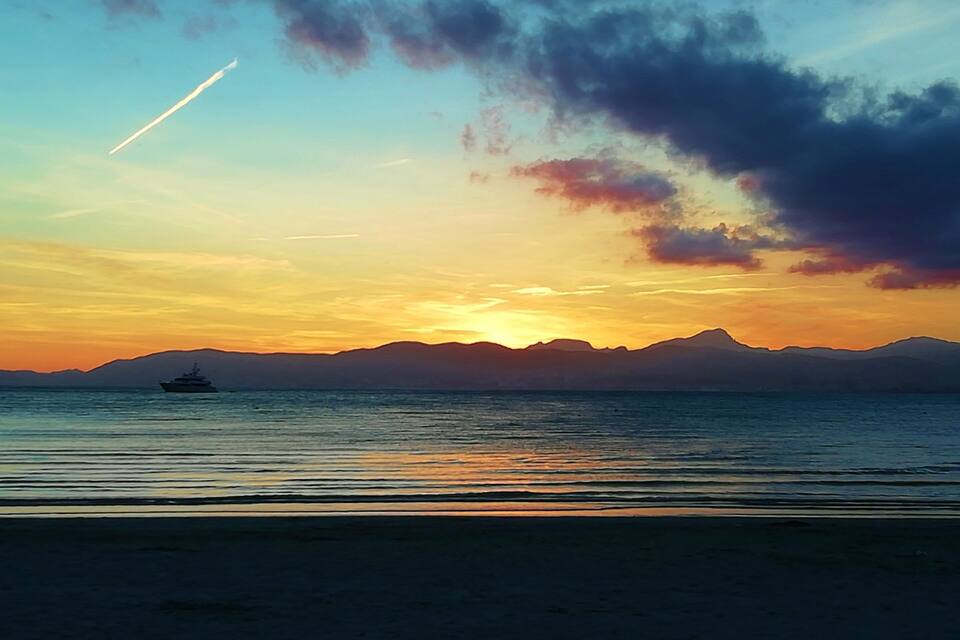 Un atardecer sobre un mar tranquilo con un yate y montañas a lo lejos.