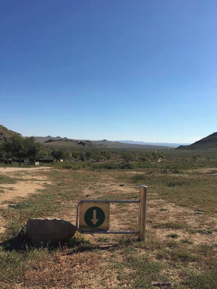 A sign with a downward arrow in a grassy field with distant hills.