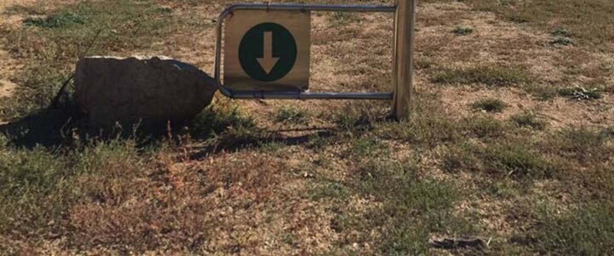 A sign with a downward arrow in a grassy field with distant hills.