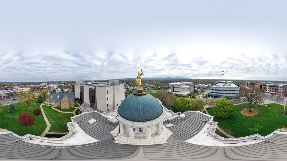 A large domed building with a golden statue on top, surrounded by green lawns and trees.
