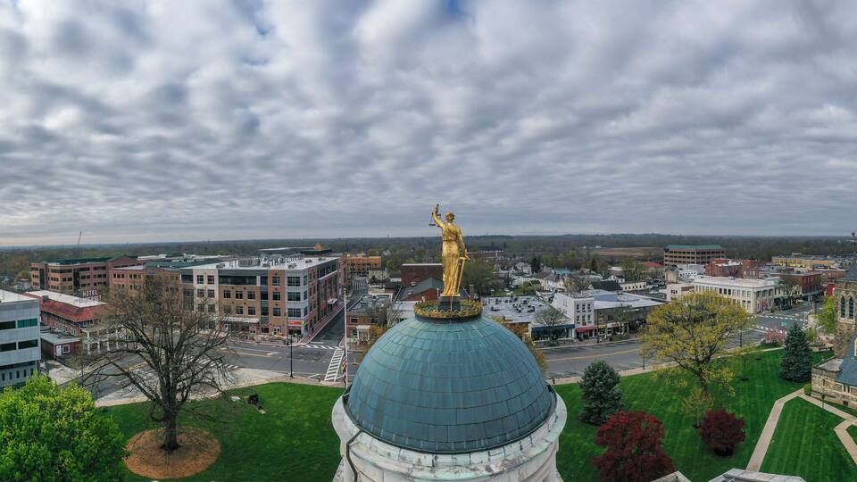 A cityscape with a prominent green dome building, a golden statue, and various modern and historic buildings.