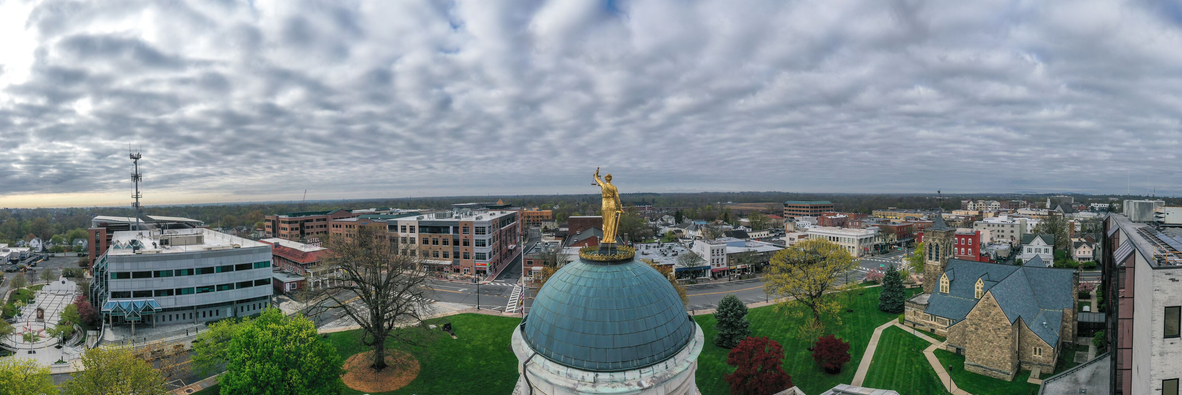 A cityscape with a prominent green dome building, a golden statue, and various modern and historic buildings.