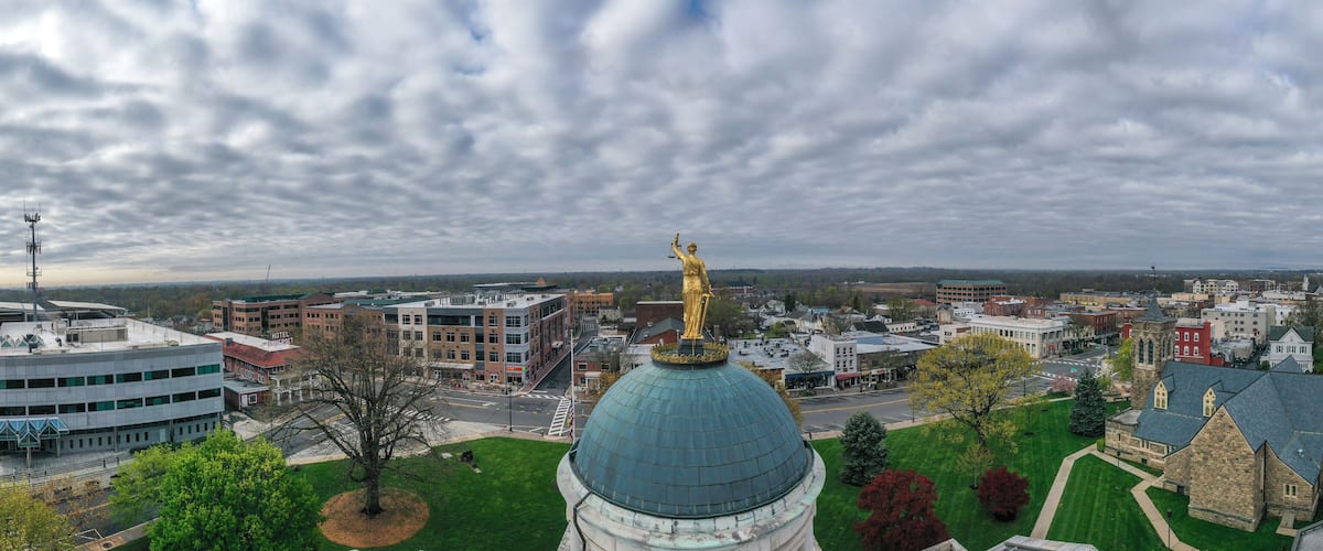 A cityscape with a prominent green dome building, a golden statue, and various modern and historic buildings.
