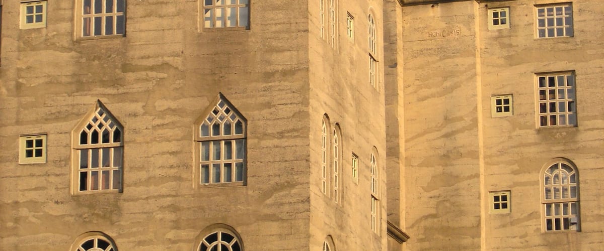 A large, historic building with multiple arched windows and a prominent weather vane on the roof.