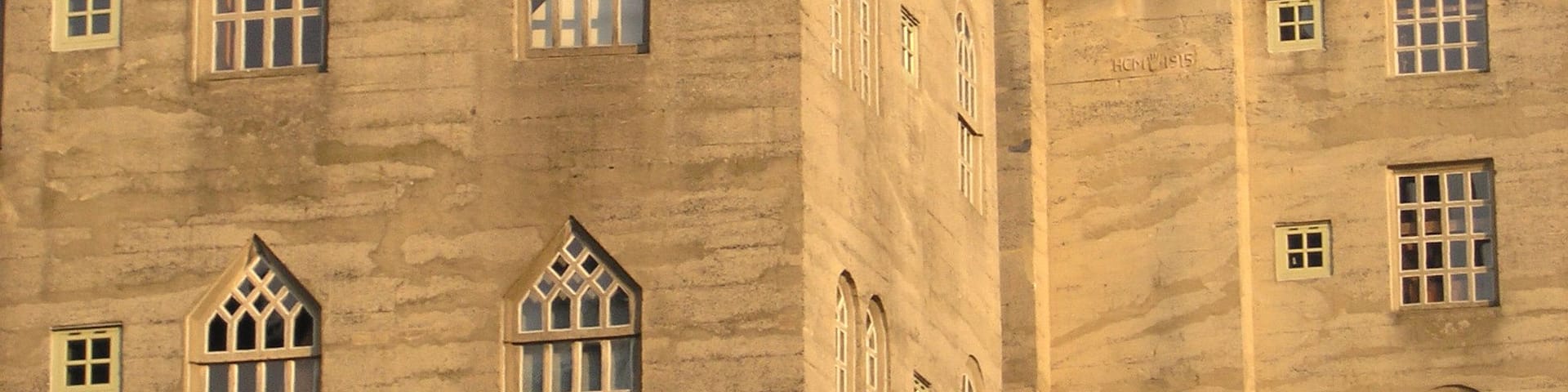 A large, historic building with multiple arched windows and a prominent weather vane on the roof.