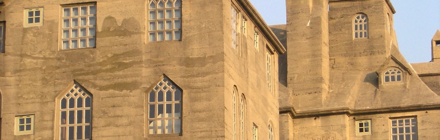 Um edifício grande e histórico com várias janelas em arco e uma girandola bem visível no telhado.