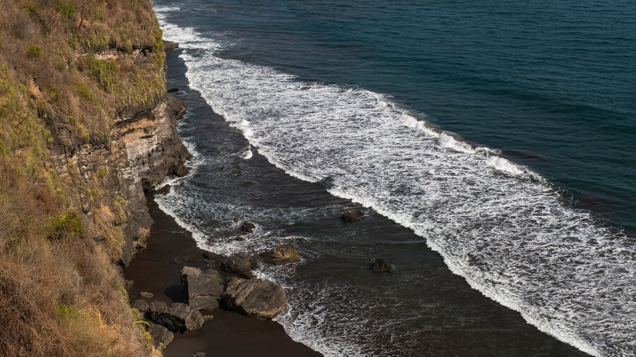 Aerial view of white foamy ocean waves, black volcanic sandy beaches and rocky cliffs. Sunny day, blue sky. Pacific coast of El Salvador.