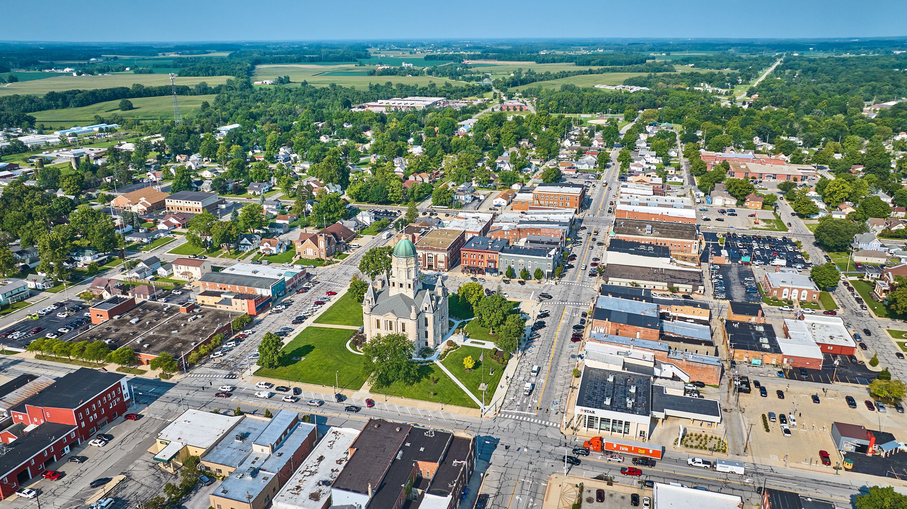 An aerial view of a town with a prominent church, a large parking lot, and surrounding green fields.