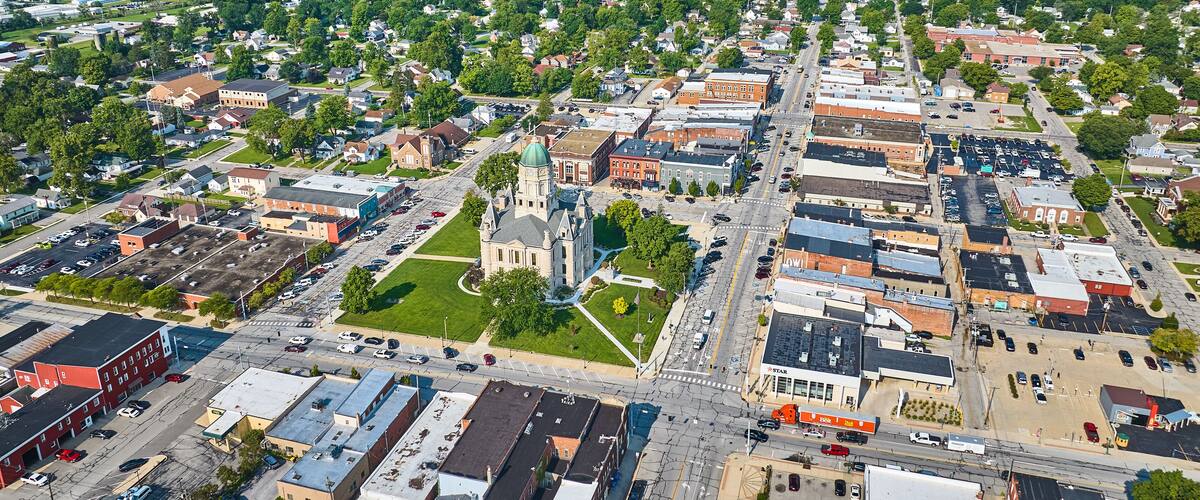 An aerial view of a town with a prominent church, a large parking lot, and surrounding green fields.