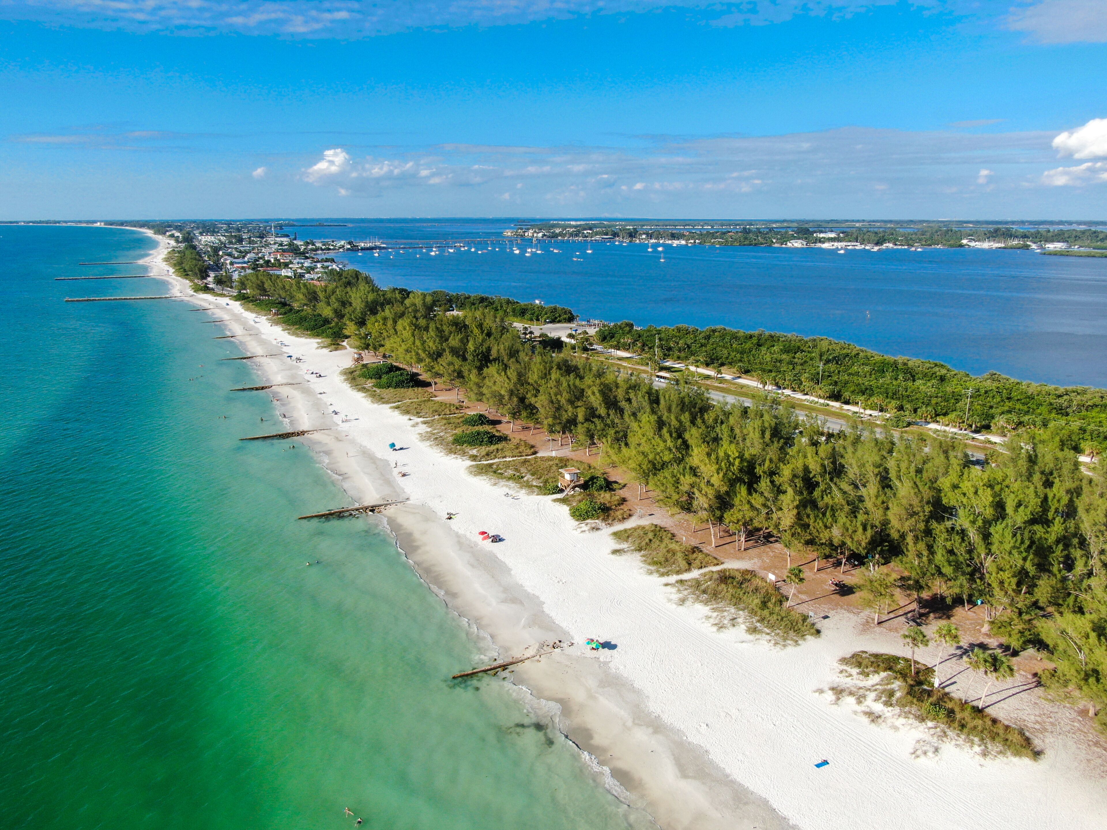 A coastal beach with clear turquoise waters, a sandy shore, and a dense forested area.