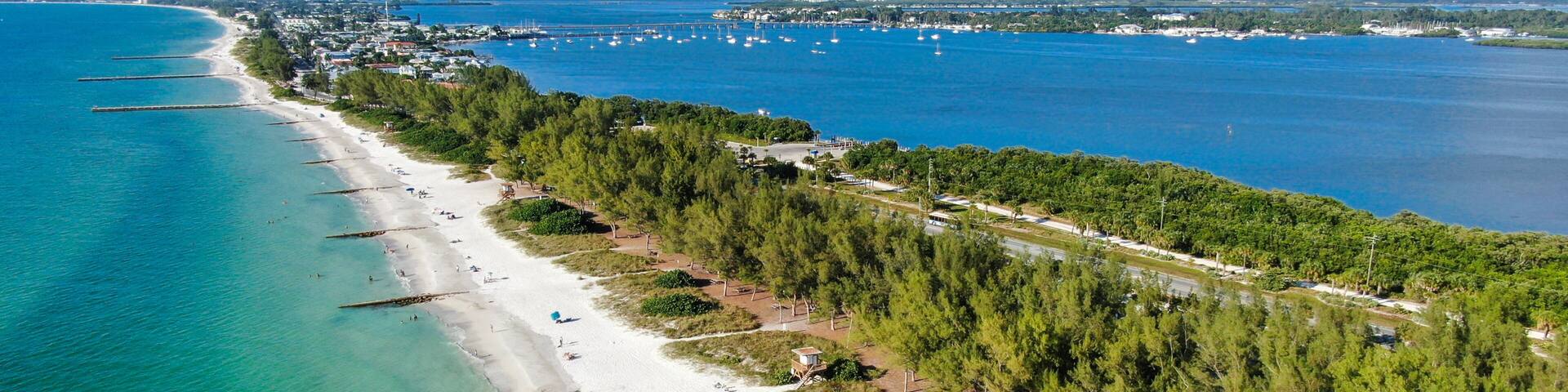 A coastal beach with clear turquoise waters, a sandy shore, and a dense forested area.