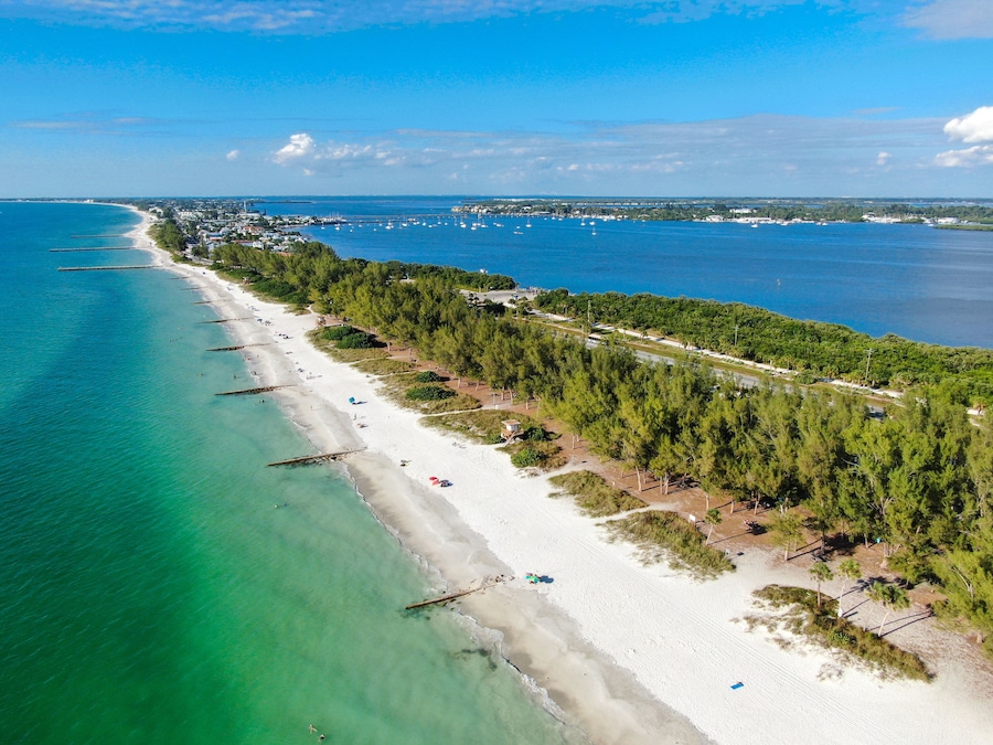 A coastal beach with clear turquoise waters, a sandy shore, and a dense forested area.