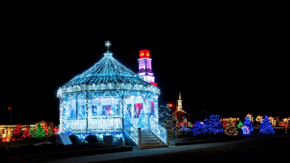 A brightly lit gazebo with a star on top, surrounded by colorful Christmas lights and trees.