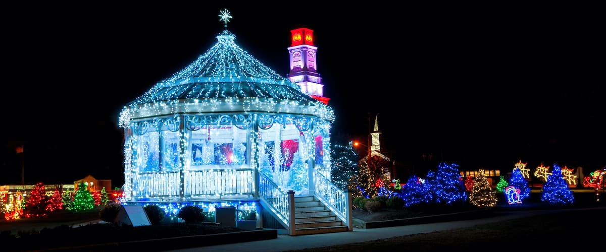 A brightly lit gazebo with a star on top, surrounded by colorful Christmas lights and trees.