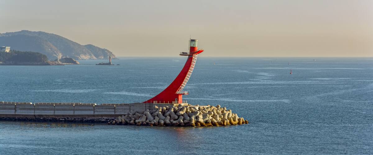 A red lighthouse on a pier with a rocky breakwater.