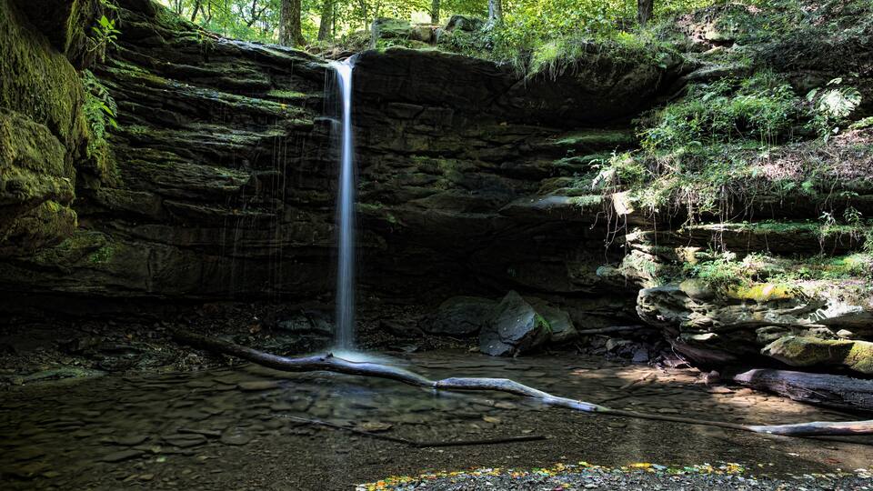 A waterfall cascading down a moss-covered rock formation surrounded by dense forest.