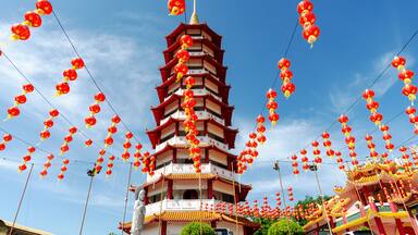A multi-tiered pagoda with red lanterns hanging from wires against a clear blue sky.