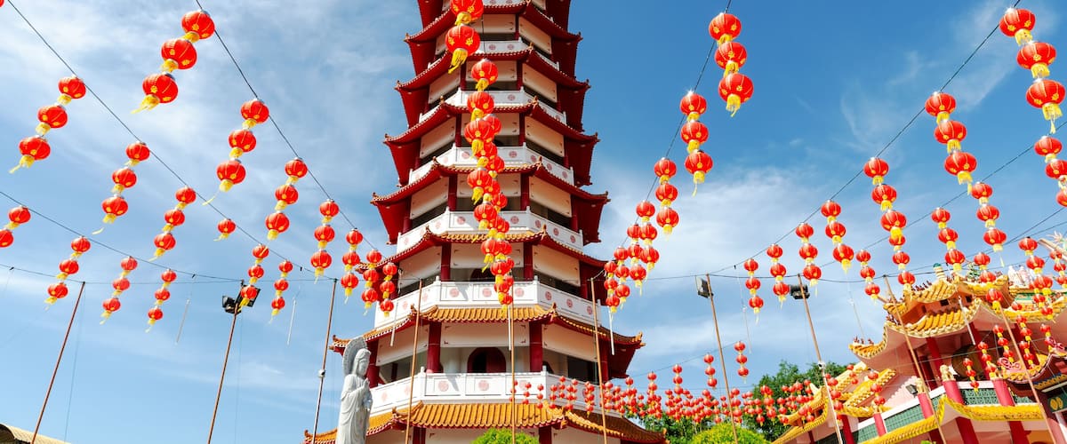 A multi-tiered pagoda with red lanterns hanging from wires against a clear blue sky.