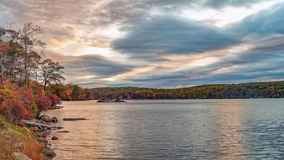 A calm lake with autumn foliage, a rocky shoreline, and a distant island.