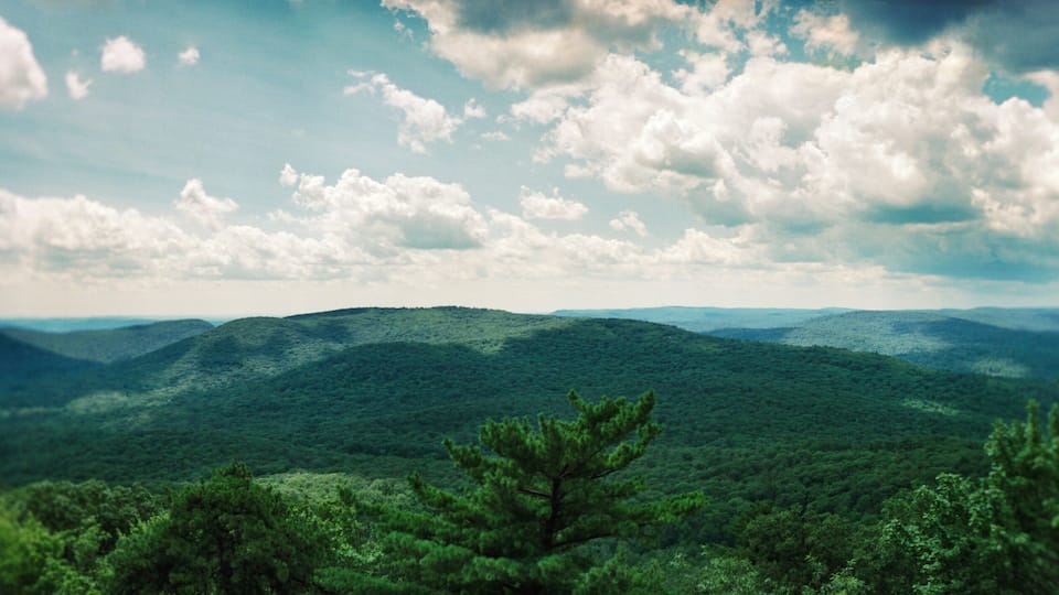 A mountainous landscape with dense forests and a partly cloudy sky.