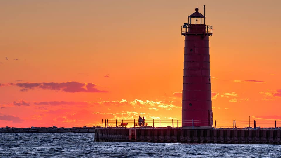 A lighthouse at sunset with a vibrant orange sky.