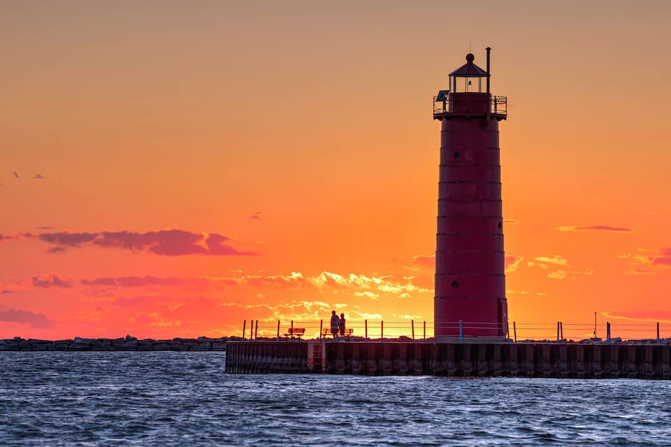 A lighthouse at sunset with a vibrant orange sky.
