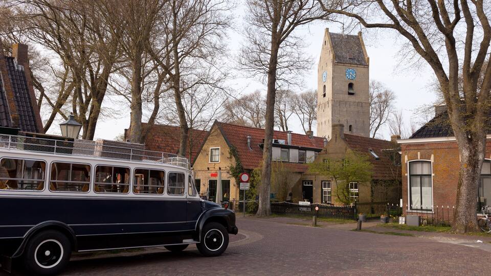 A vintage bus parked on a cobblestone street, a church with a clock tower, and traditional European architecture.