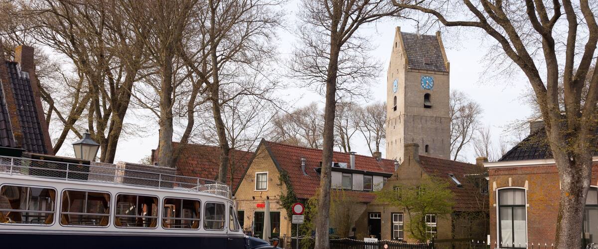 A vintage bus parked on a cobblestone street, a church with a clock tower, and traditional European architecture.