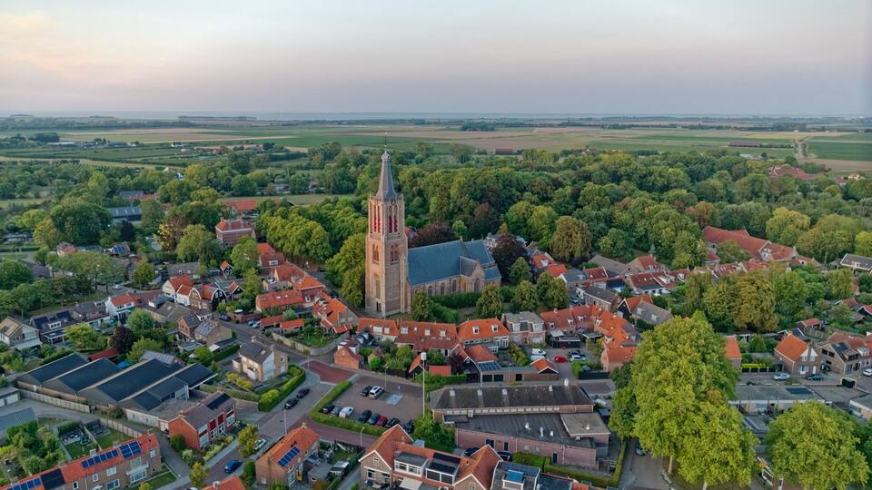 An aerial view of a town with a prominent church tower, surrounded by residential buildings and lush greenery.
